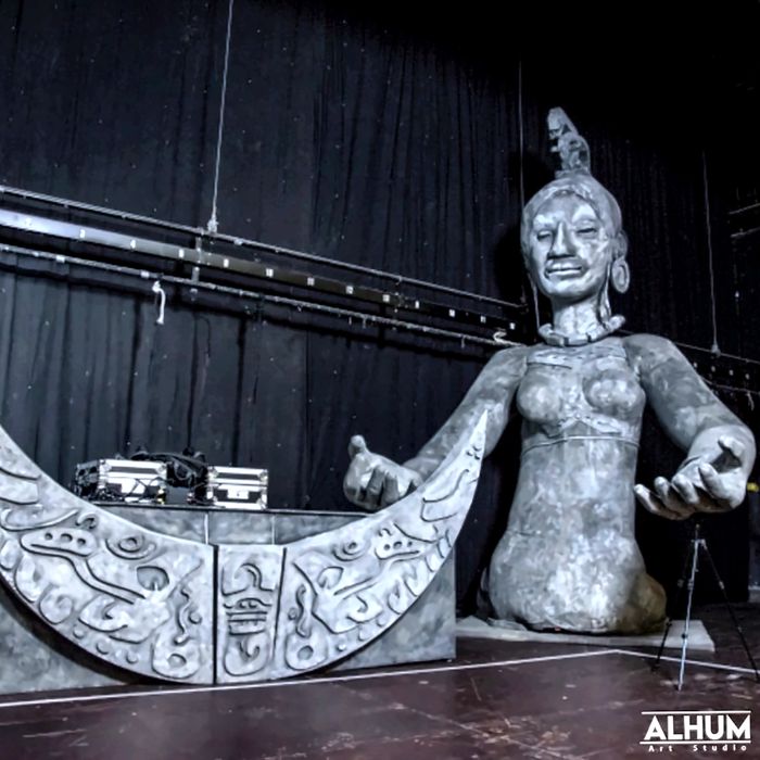 Escultura de figura maya junto a una cabina de DJ en forma de luna tallada